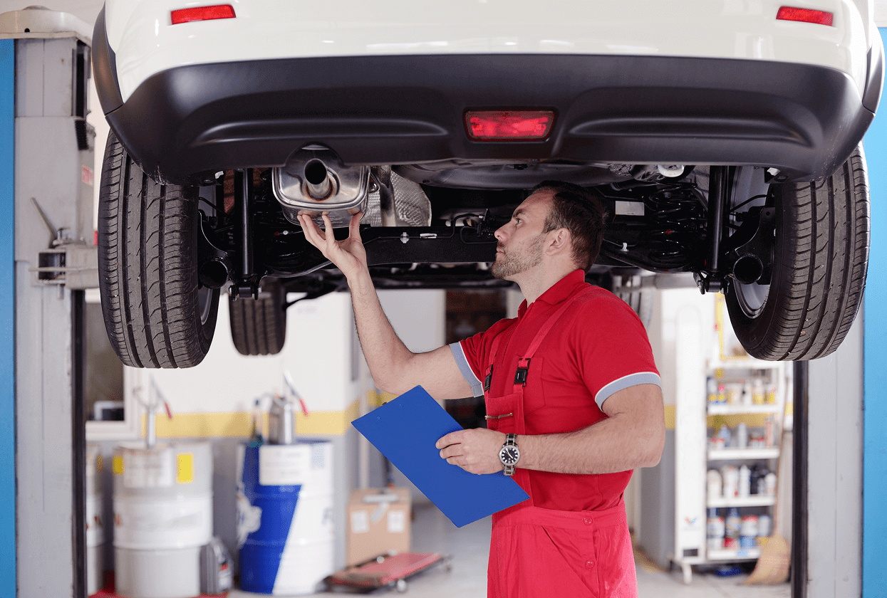Mechanic inspecting car exhaust in garage.