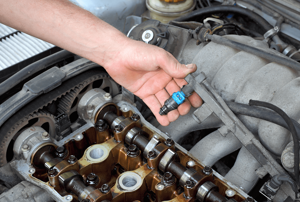 Hand holding fuel injector in car engine.