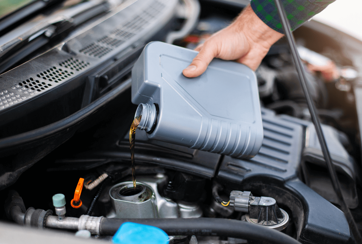 Hand pouring oil into car engine.