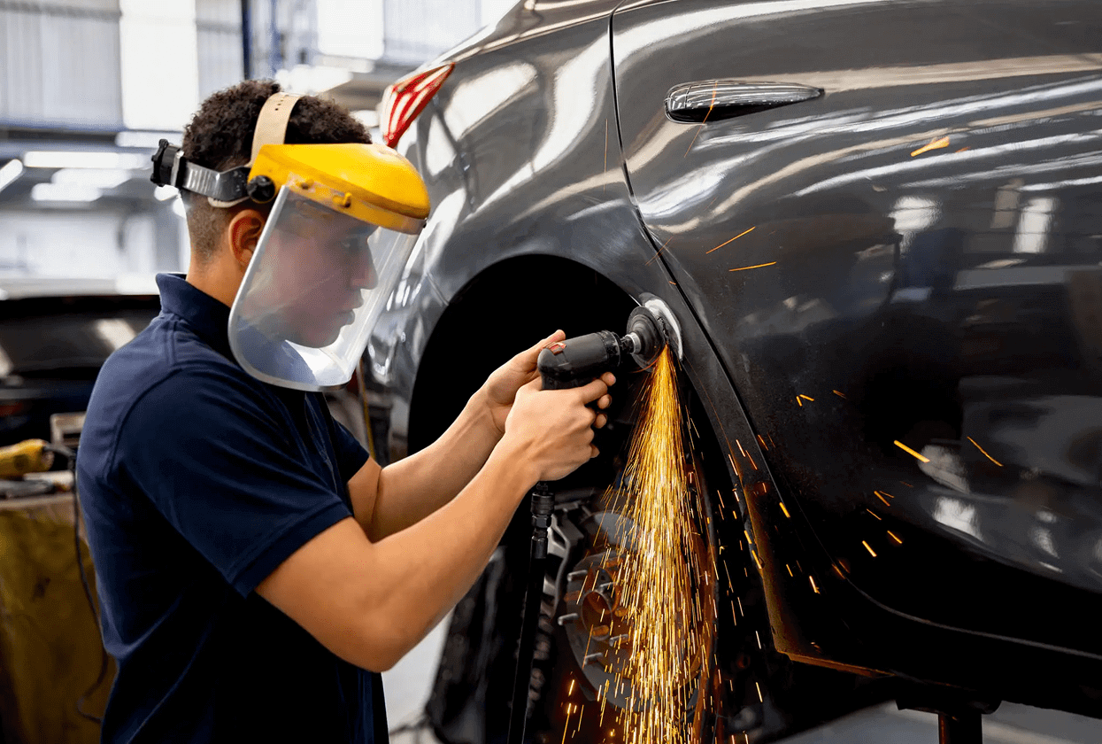 Worker using grinder on car body with safety gear.